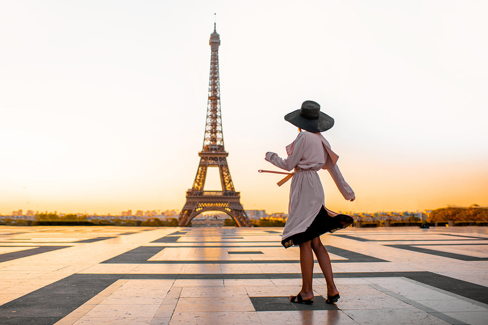 a chic woman in a hat standing in front of the Eiffel Tower at sunset