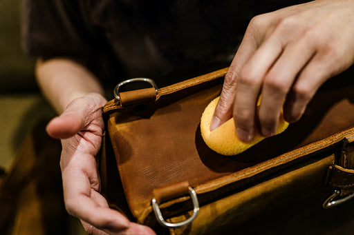 a cleaning sponge being used on a leather bag