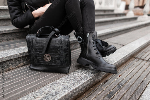 a close up of a woman’s black outfit, with black leather boots and croc patterned purse