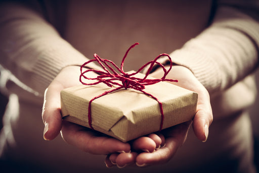 a close up of hands holding a handmade gift wrapped in brown paper and red string