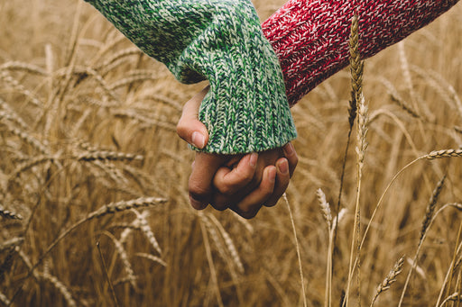 a close up of two people holding hands in a corn field
