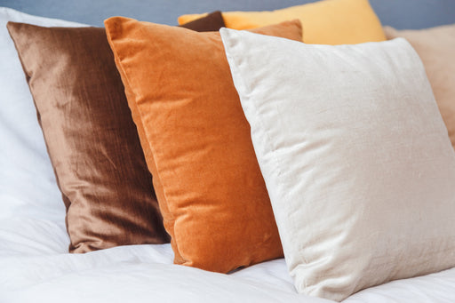 a collection of velvet cushions in brown, rust and off white colors