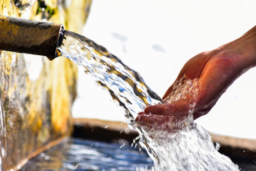 a hand in a stream of clear water flowing from a trough