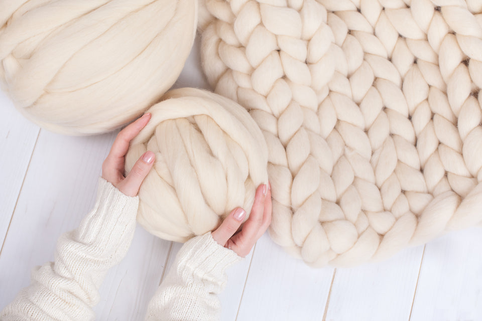 a large cream knitted rug and cream balls of wool