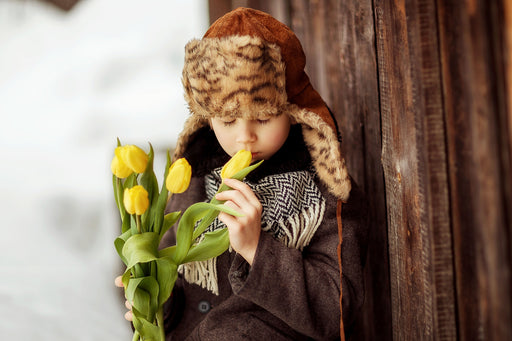 a little boy wearing a faux fur hat smelling some yellow tulips