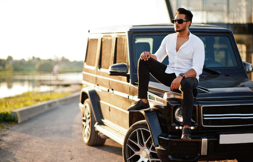 a man sitting on his SUV wearing a white open neck button shirt