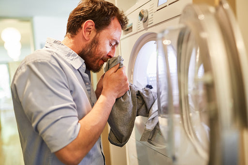 a man standing by the washing machine smelling freshly laundered clothing