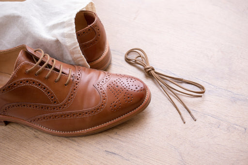 a pair of brown leather brogues, one still in its dust bag