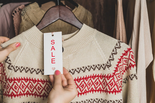 a patterned cream sweater on a wooden hanger with a sale ticket attached to it
