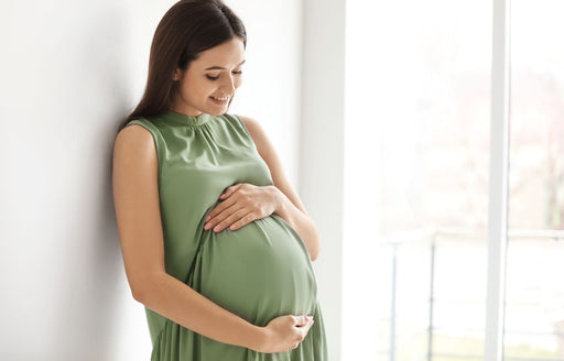 a smiling pregnant woman in a sleeveless sage green dress caressing her bump