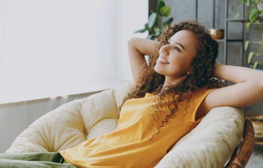 a smiling woman leaning back in her chair, wearing a yellow tee and green pants