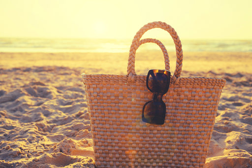 a straw tote bag and sunglasses on a beach