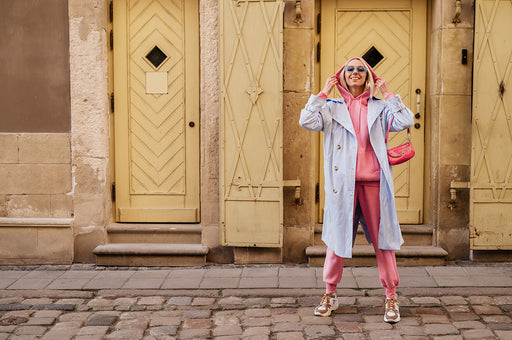 a stylish outfit consisting of pink sportswear under a lilac mac, with matching pink purse and plain sneakers