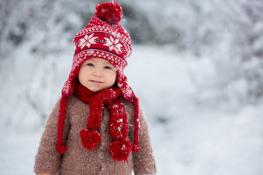 a toddler in the snow, wearing a cozy woolen red bobble hat and scarf