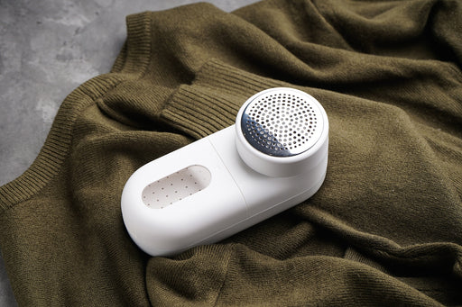 a white fabric shaver lying on an olive green sweater
