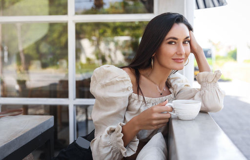 a woman drinking her coffee wearing a boat neck top with puffed sleeves