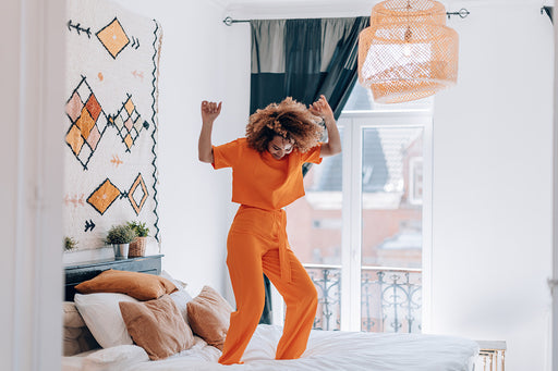 a woman having fun bouncing on her bed wearing a matching orange top and pants