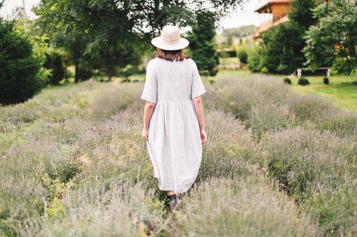 a woman in a linen dress walking through a lavender field