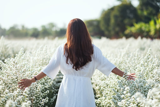 a woman in a white dress with her back to the camera in a field of white flowers