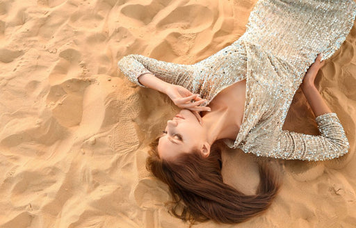 a woman lying in the sand wearing a long sleeved silver sequin dress