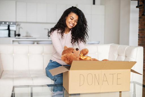 a woman putting a teddy bear in a box labelled donate