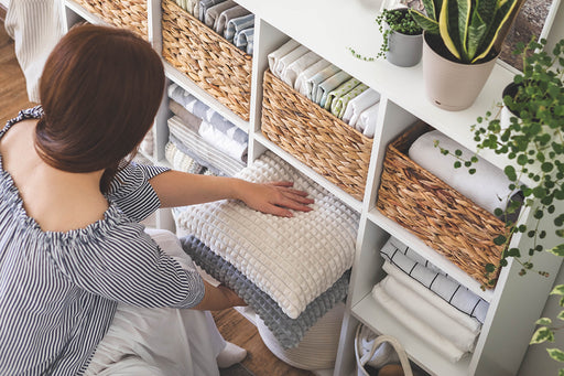 a woman putting cushions, and linens away on shelves and in straw baskets