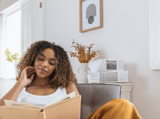 a woman reading her book with her Hayden Hill storage bags on a shelf behind her