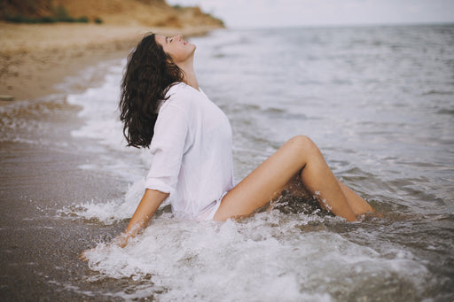 a woman relaxing in the shallow waves whilst sitting on the shoreline of the beach