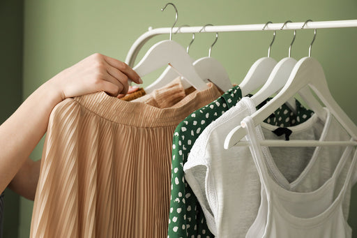a woman’s hand choosing items of clothing from a hanging rail
