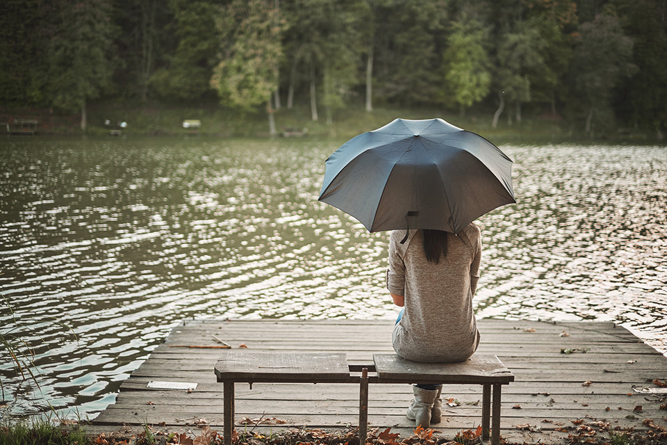 a woman sitting on a dock by a lake with an umbrella