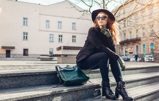 a woman sitting on steps wearing an autumnal outfit with green leather gloves and bag