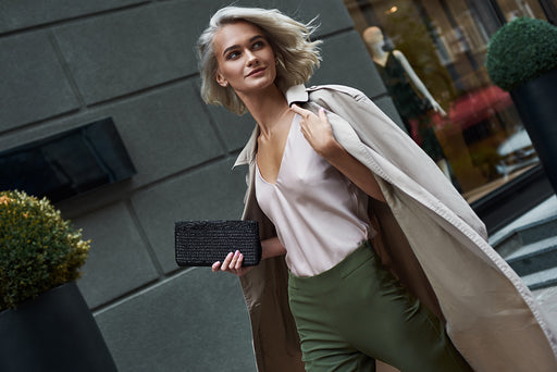 a woman walking past fashion stores dressed in green sleek trousers, silky top and mac