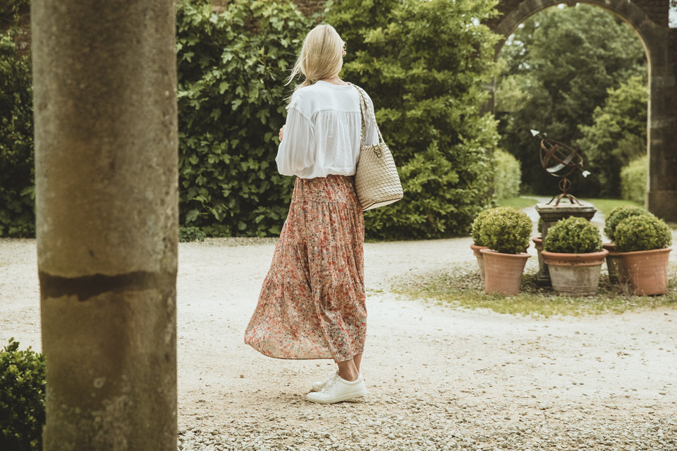 a woman wearing a beautiful patterned floaty skirt teamed with a white shirt and white pumps