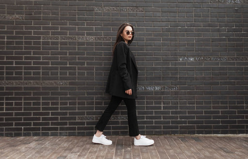 a woman wearing a black blazer and pants with white trainers