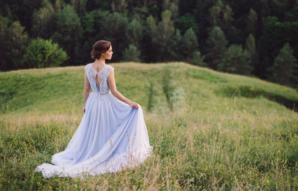 a woman wearing a pastel blue gown standing in a field