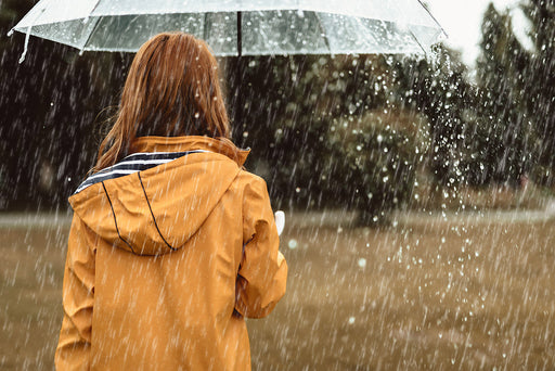 a woman wearing a raincoat under an umbrella in heavy rain