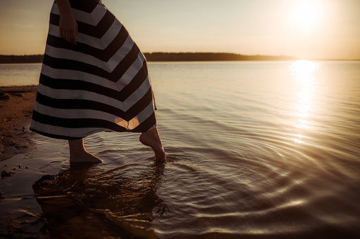 a woman wearing a striped skirt dipping her toe into the sea at sunset