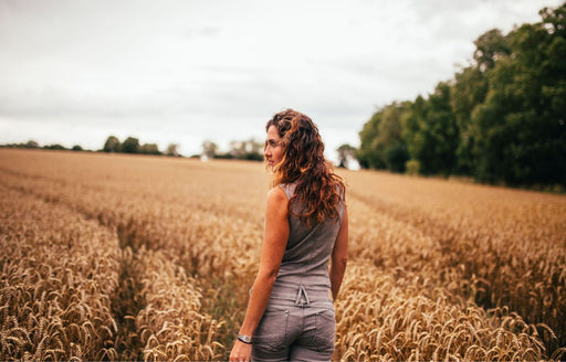 a woman wearing a stylish gray jumpsuit walking through a field of barley