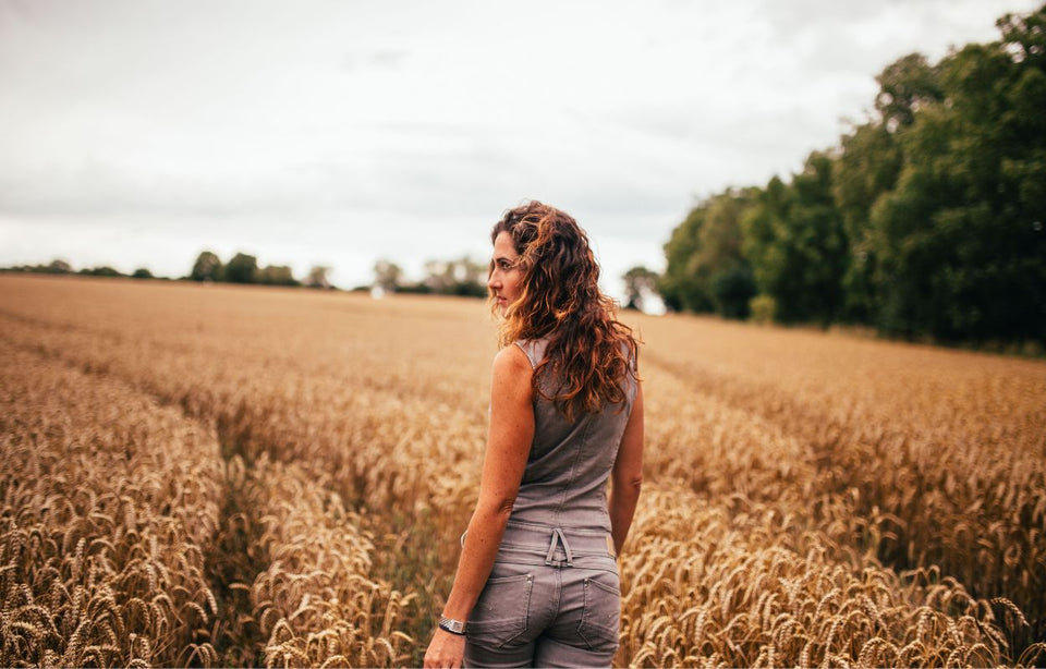 a woman wearing a stylish gray jumpsuit walking through a field of barley
