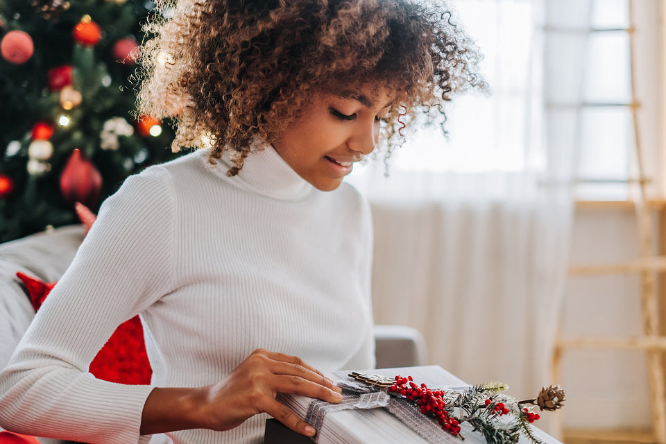a woman wearing a white turtleneck, looking at her Christmas gift