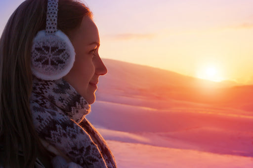 a woman wearing patterned ear muffs looking out on a scenic sunset