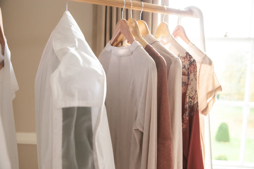 a wooden clothing rack with tops and dresses on wooden hangers