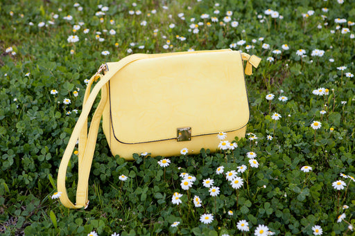 a yellow handbag on a lawn of clover and daisies
