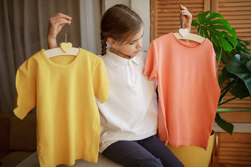 a young girl holding up a yellow and an orange t-shirt, trying to choose one of them