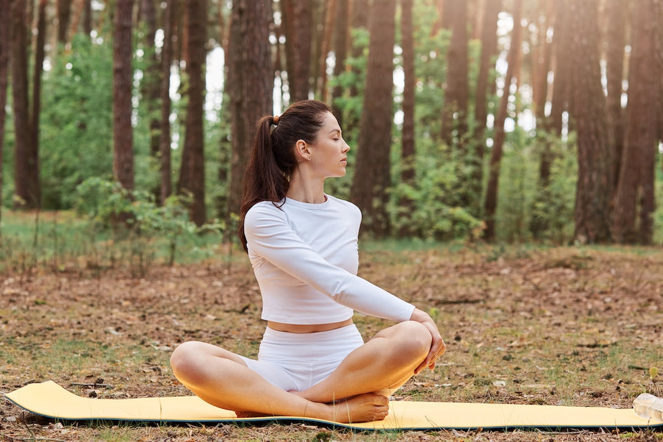 a woman outdoors practising yoga on her mat wearing a white stretch top and shorts