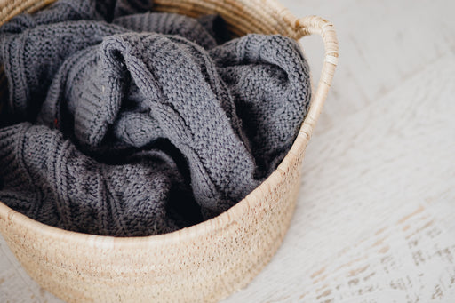 a dark grey woollen blanket in a wicker laundry basket