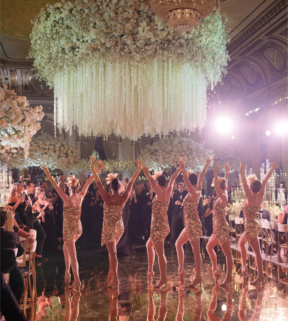A glamorous line up of dancers under an enormous floral chandelier at the Plaza Hotel, New York