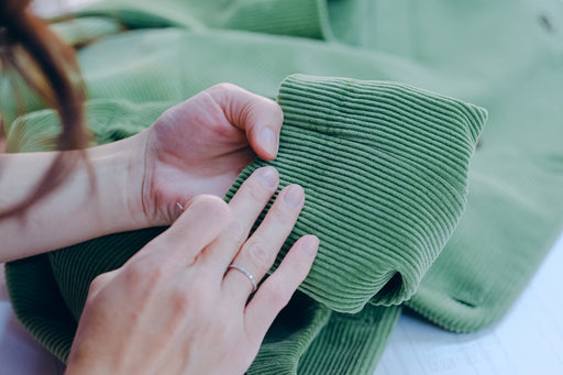 hand sewing a hem on a green corduroy jacket