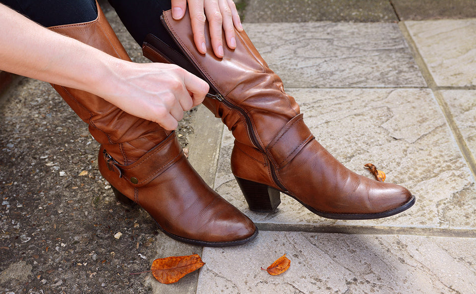 hands pulling up a zip on a pair of brown leather boots