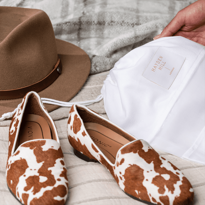 a close up of pony skin print pumps and a dust bag next to a felt hat on a bed